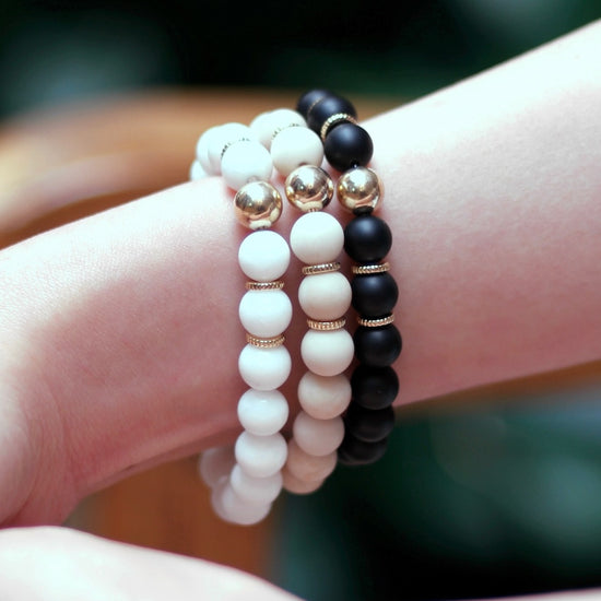 Beaded bracelet stack on female model's wrist wearing Neutra Black Onyx, White Jade, and Natural Fossil gemstones.