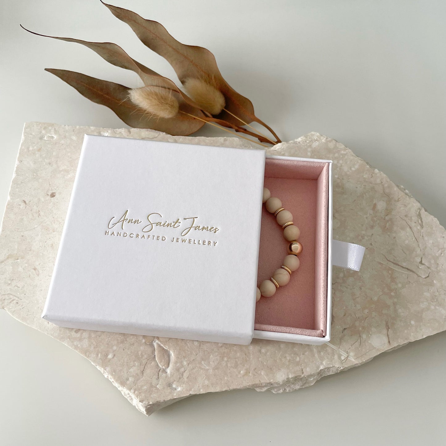 Ann Saint James packaging with natural gemstone beaded bracelet made of Natural Fossil crystal and 14k gold-filled metal over limestone slab.