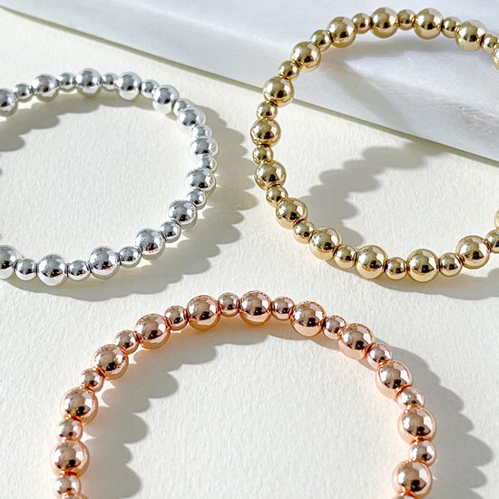 Flat-lay of beaded bracelets stacked together with Alterner Hematite gemstone bracelets in silver, gold and rose gold tones.